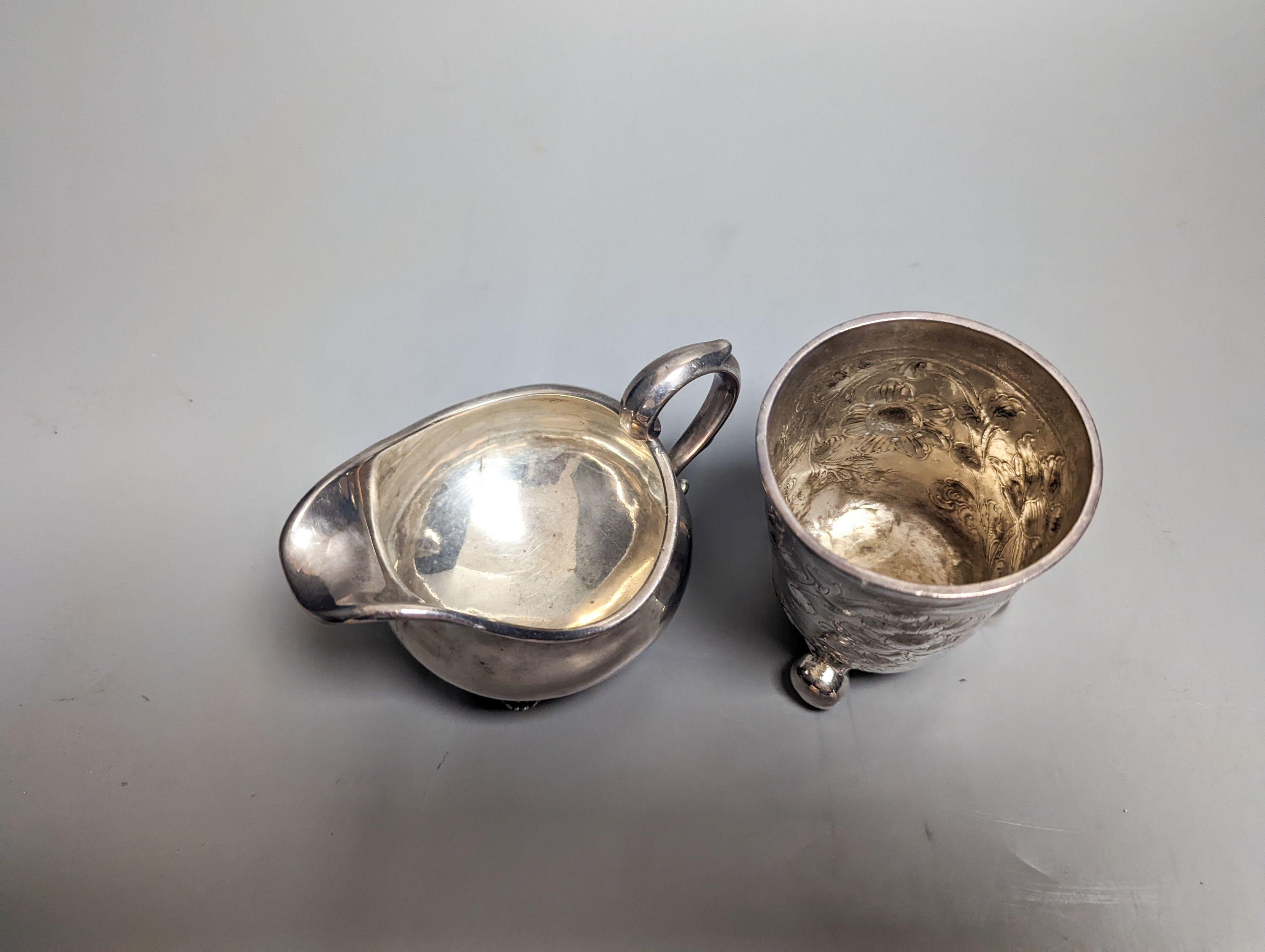 A William IV provincial silver cream jug, Barber & North, York?, 1836 and an 18th century continental embossed white metal beaker(a.f.), gross 6.5oz.